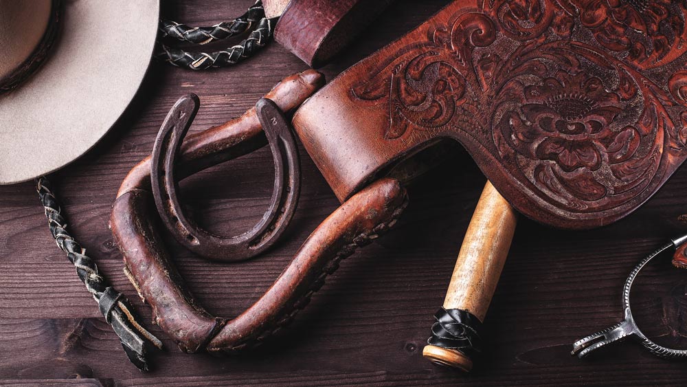 Background image of a western saddle, cowboy hat, horseshoe, and whip