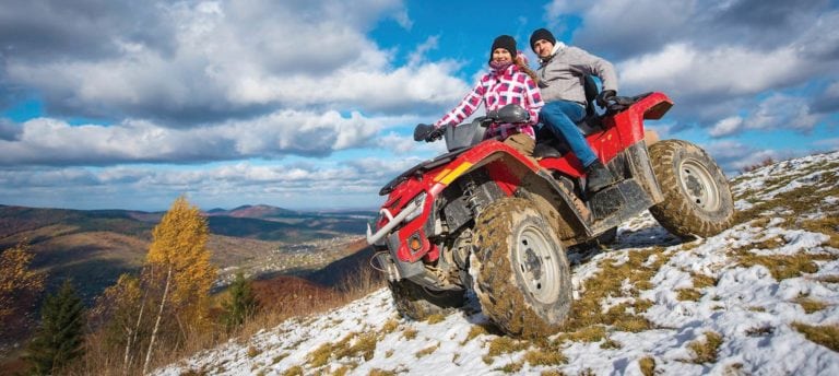 Couple in winter clothes riding on a red atv