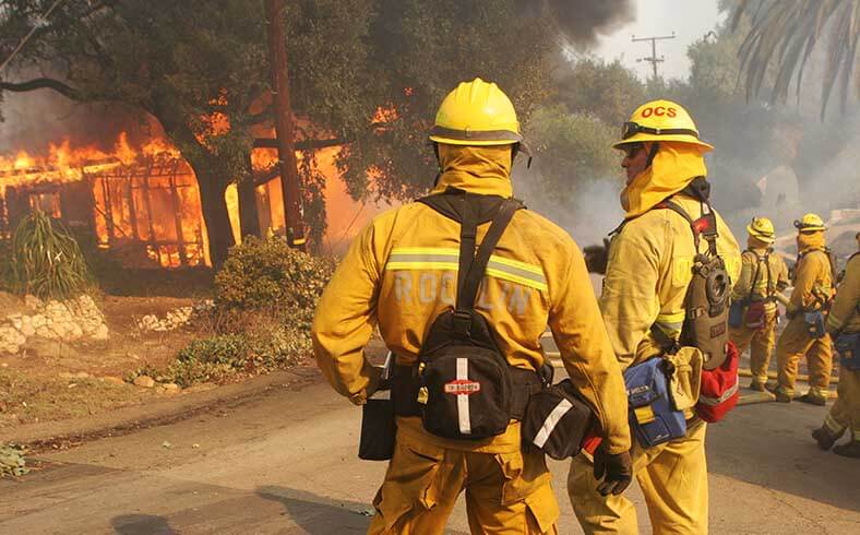 Firefighters watch a home burn down during the Harris Ranch fire around Lake Hodges, California