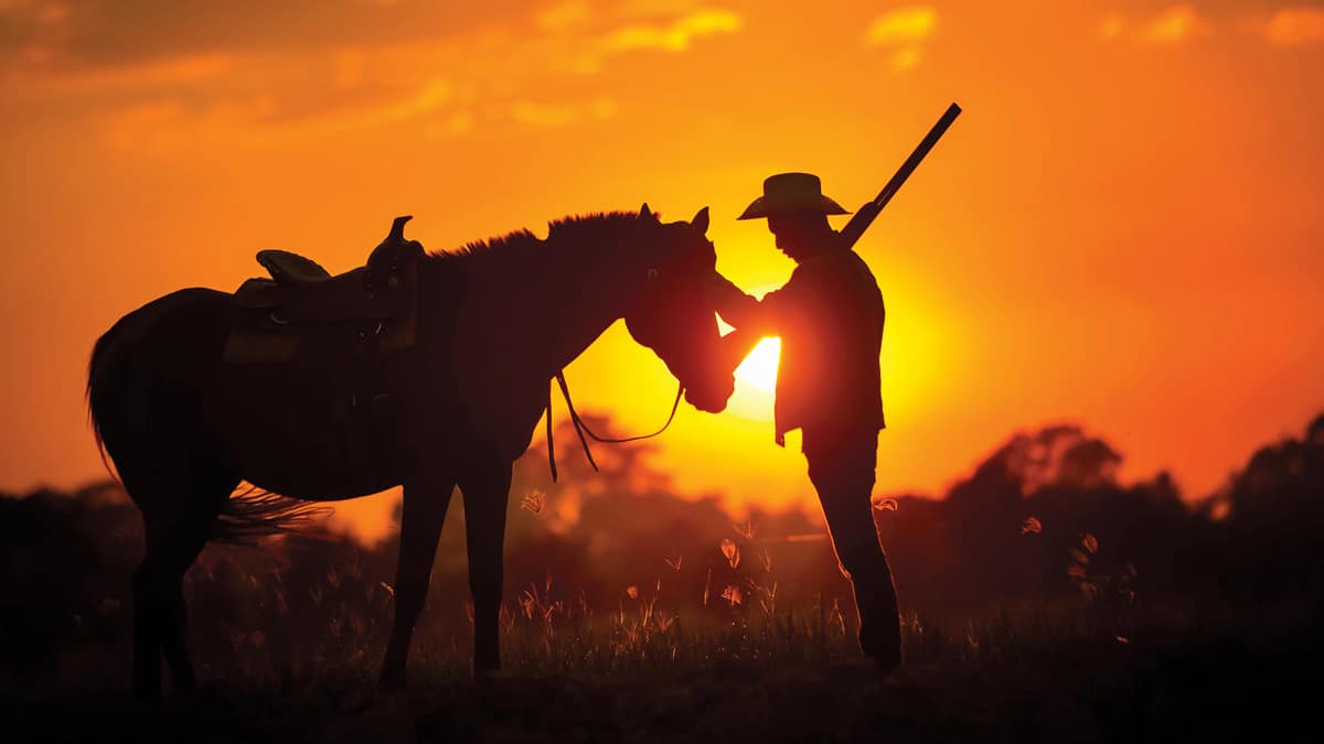 Cowboy with rifle caressing horse