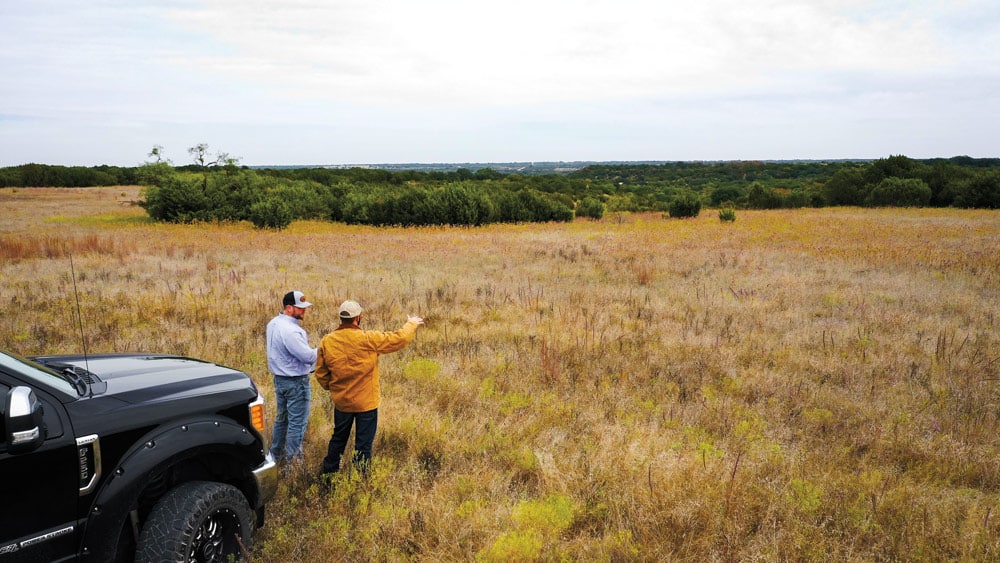 two men standing next to a truck on a tract of land