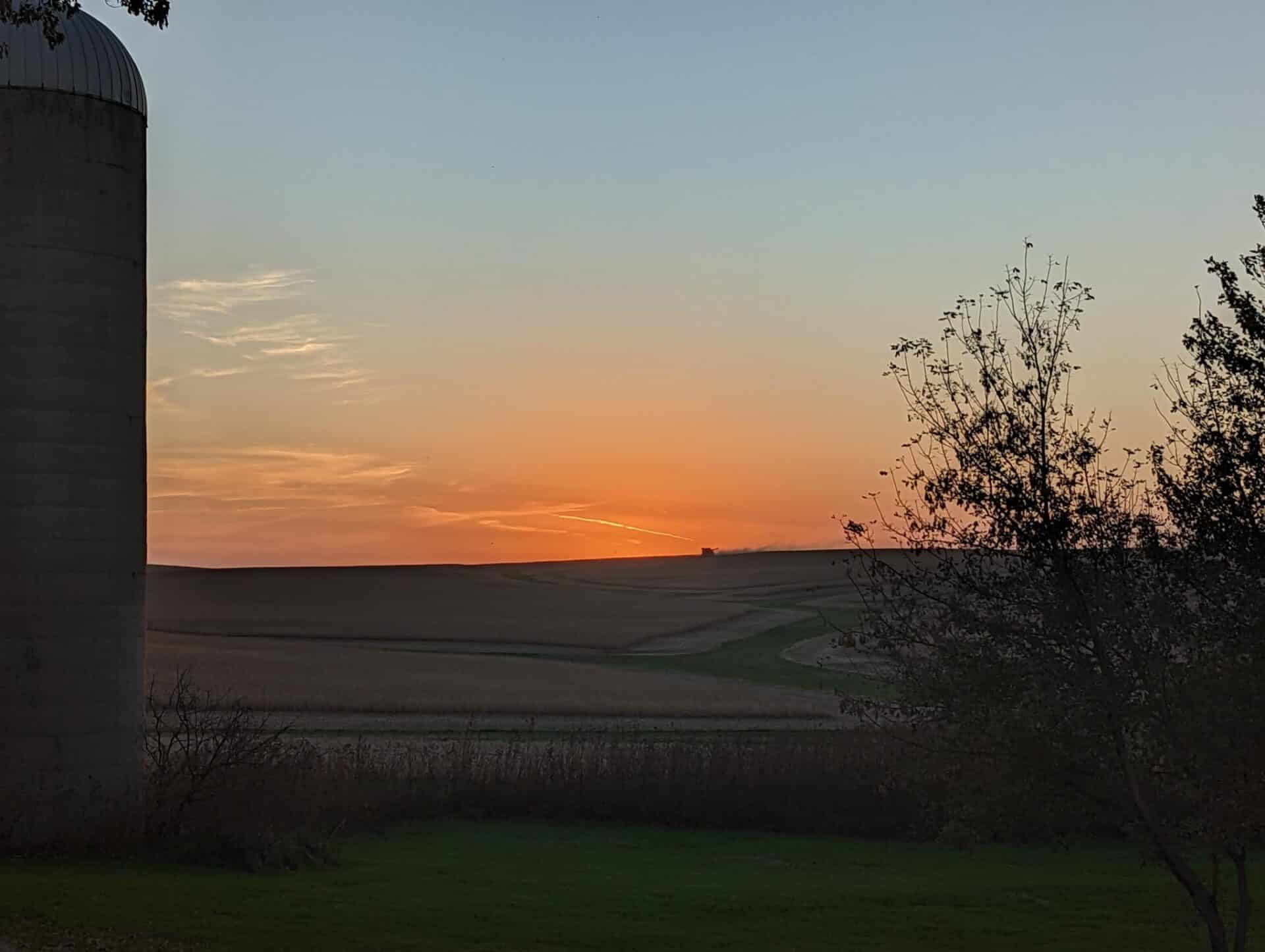 Tractor harvesting crops on the horizon as the sun sets
