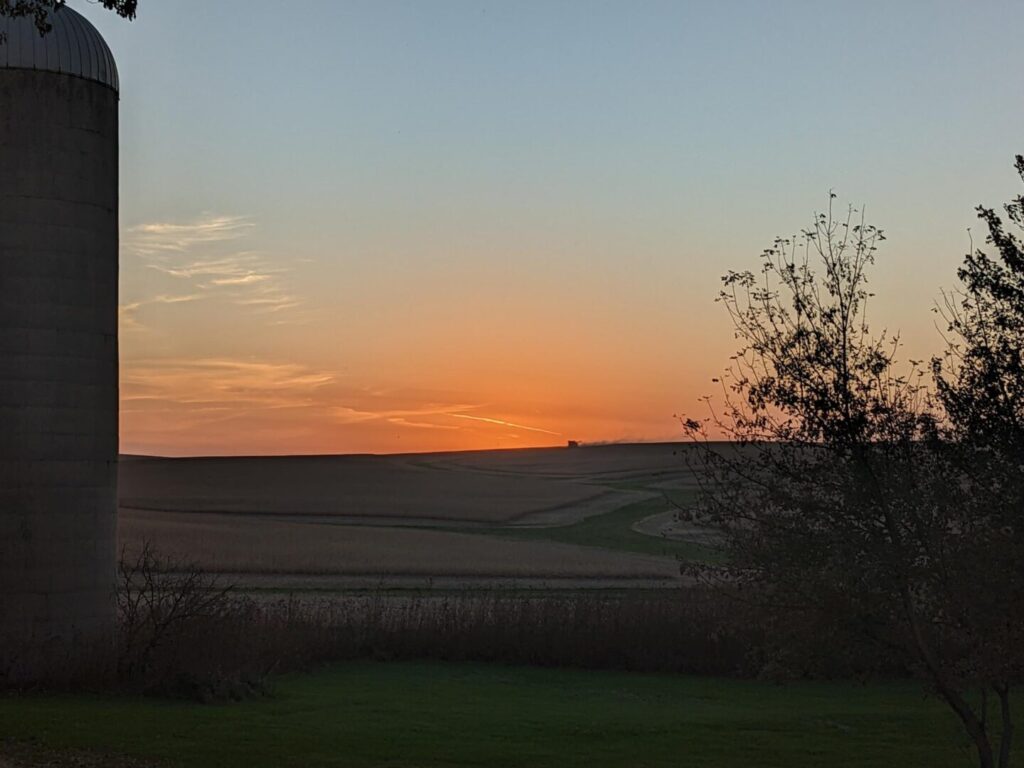 Tractor harvesting crops on the horizon as the sun sets