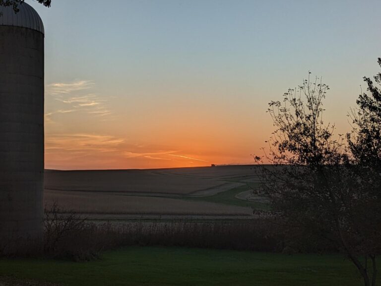 Tractor harvesting crops on the horizon as the sun sets